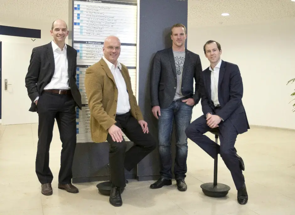 Vier Personen im Foyer eines Bürogebäudes, im Hintergrund eine Firmentafel