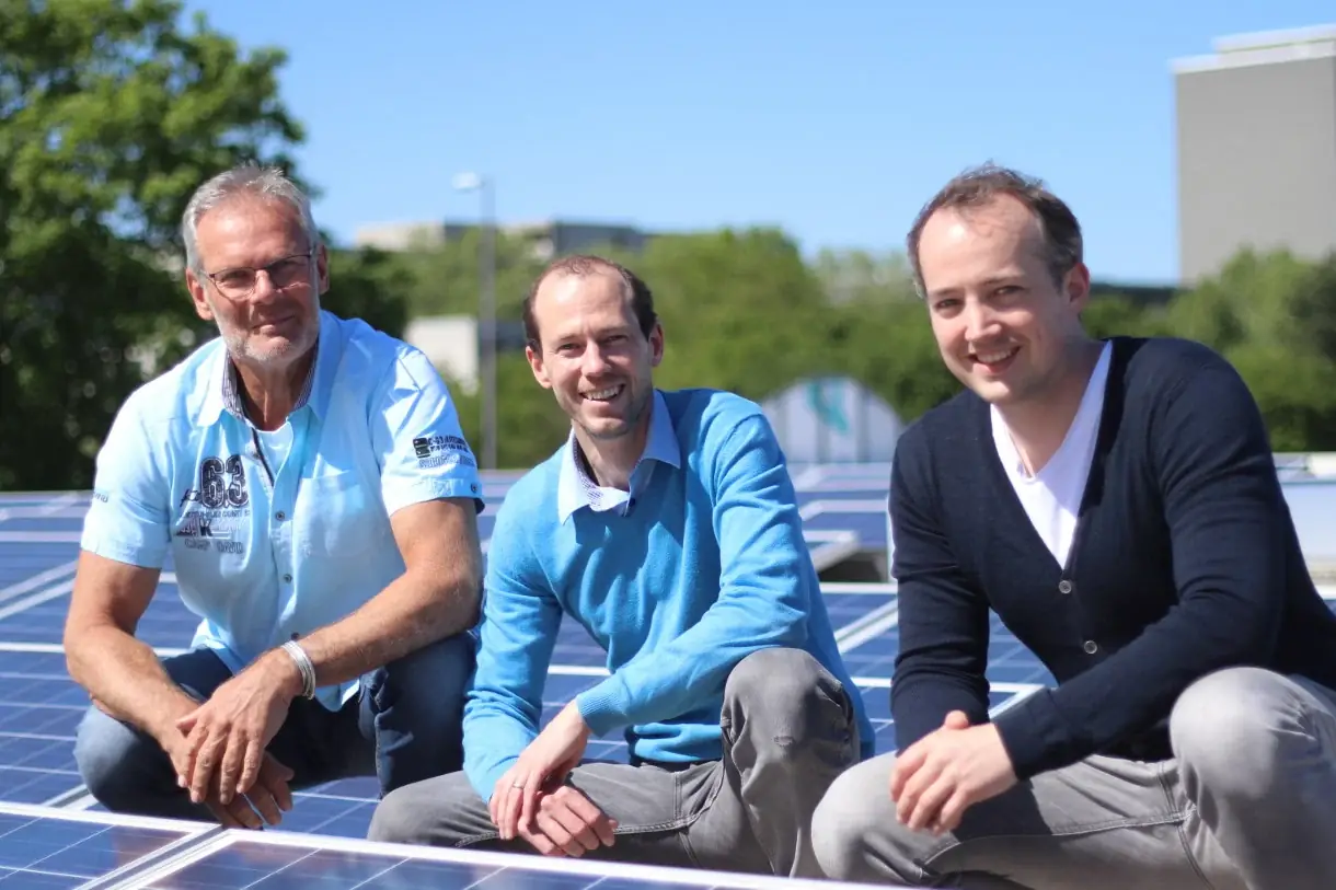 Drei Personen sitzen nebeneinander auf einer Photovoltaikanlage auf einem Flachdach